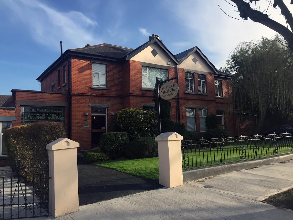 Cahill Dental Clinic at 108 St Mobhi Road: a red-brick house with two cream gables, a front lawn and an oval hanging sign